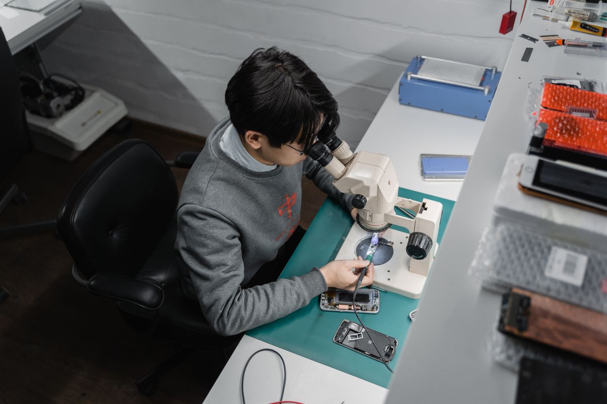 Foto ilustrativa de técnico examinando um celular em bancada de manutenção